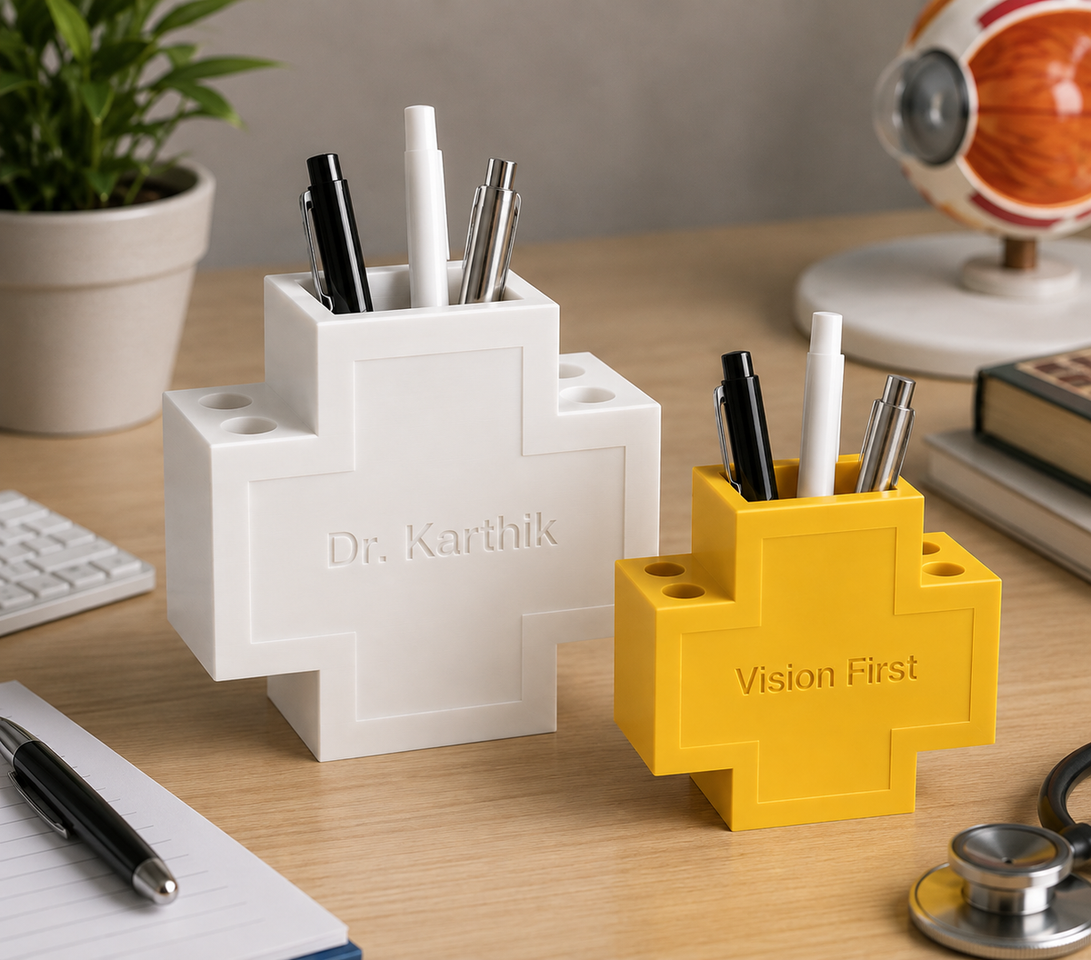Two cross-shaped desk organizers in white and yellow, styled on a wooden desk with pens inside. The white one is engraved with 'Dr.